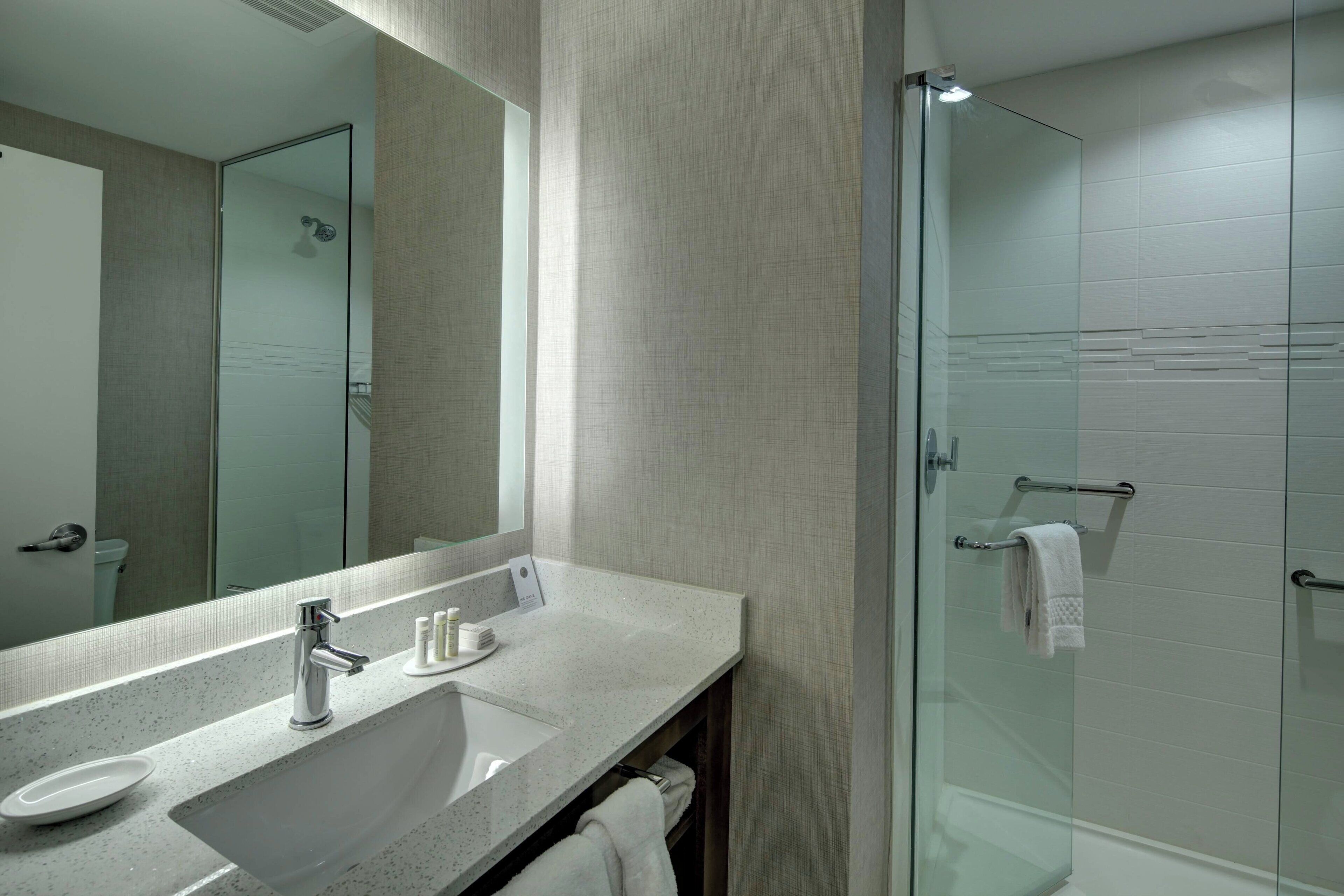 A modern bathroom with a large mirror, a sink, and a glass shower enclosure.