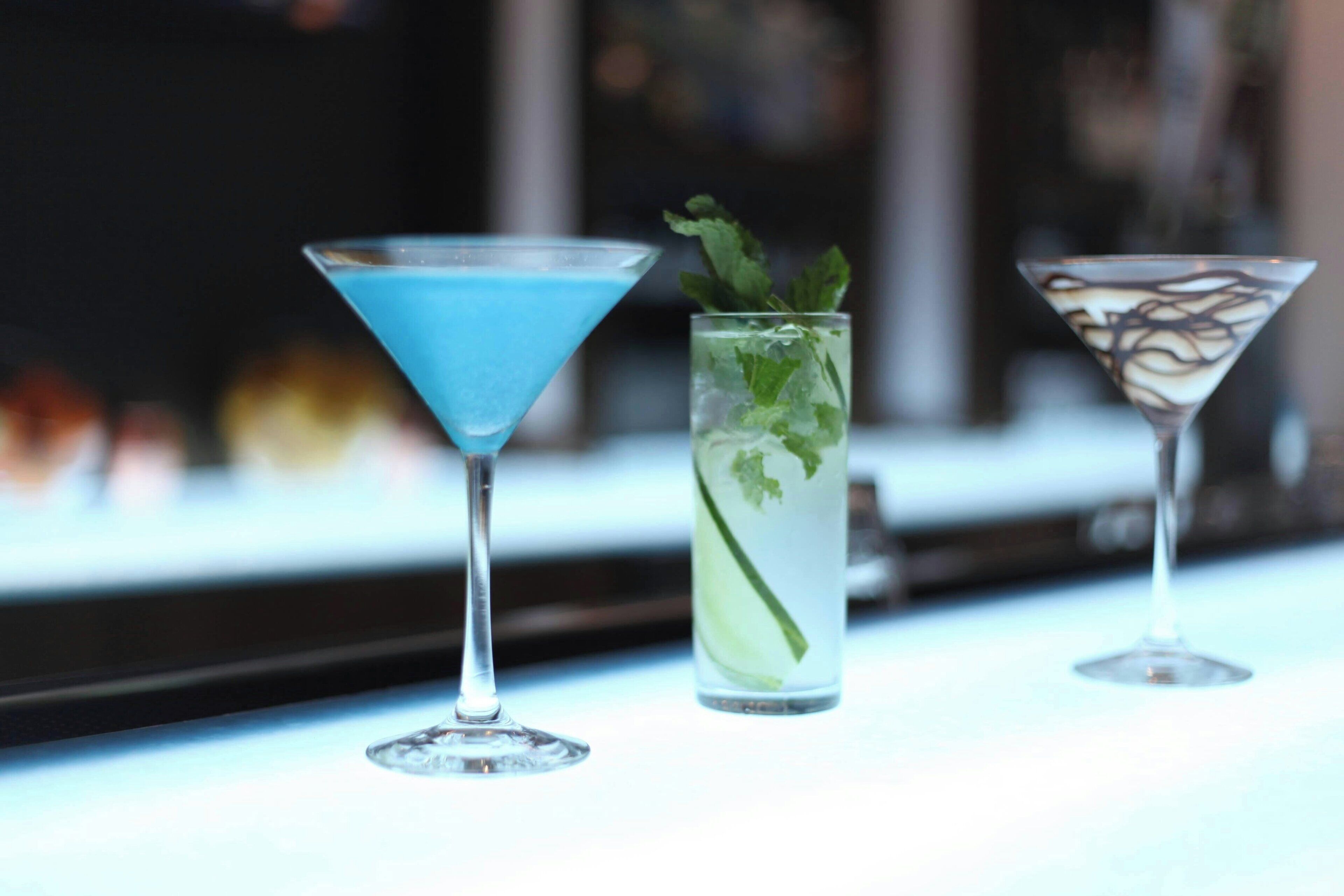 Three cocktails in martini glasses on a bar counter.