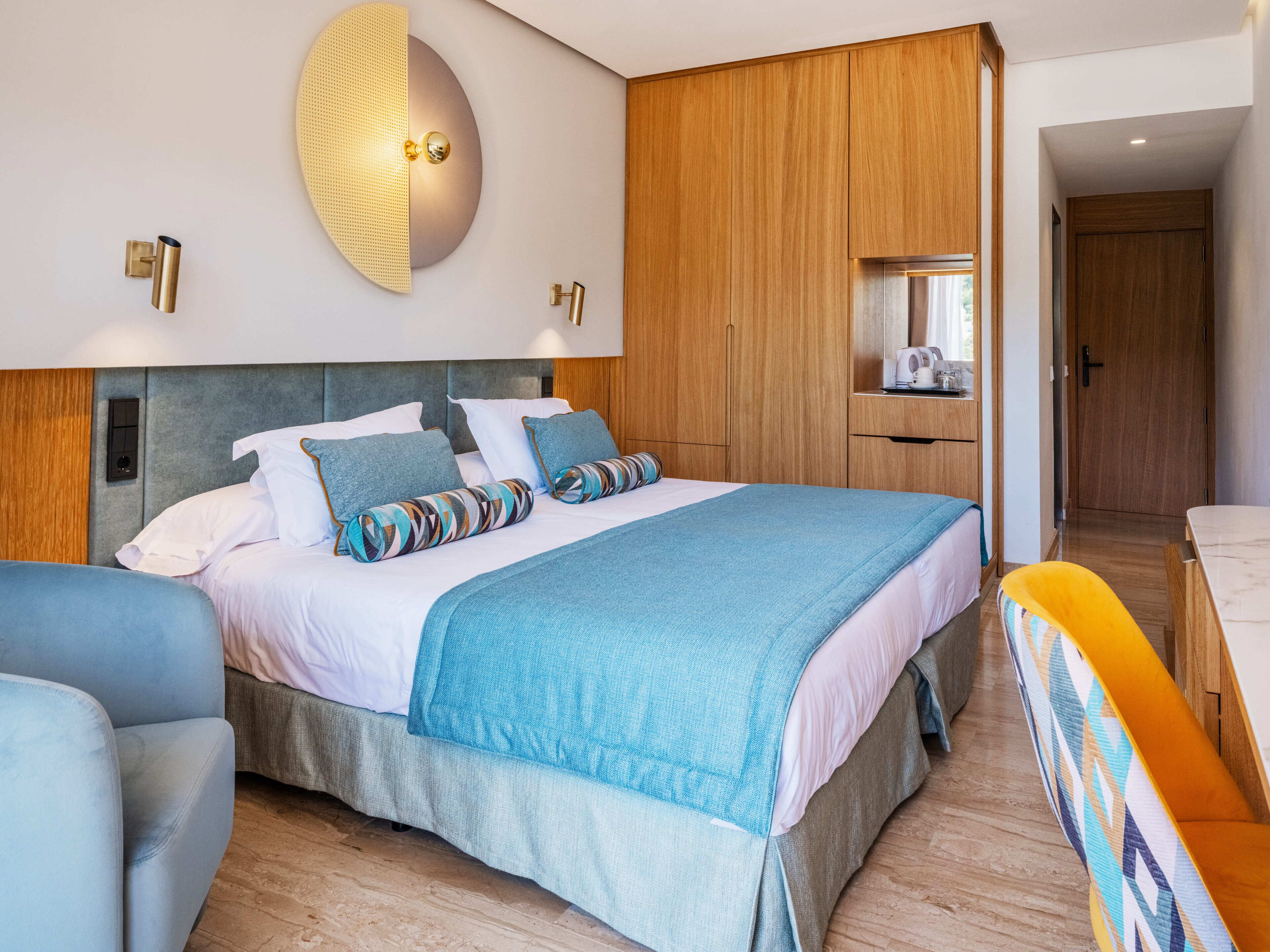 A modern hotel room with a large bed, wooden wardrobe, and a bathroom visible through an open door.