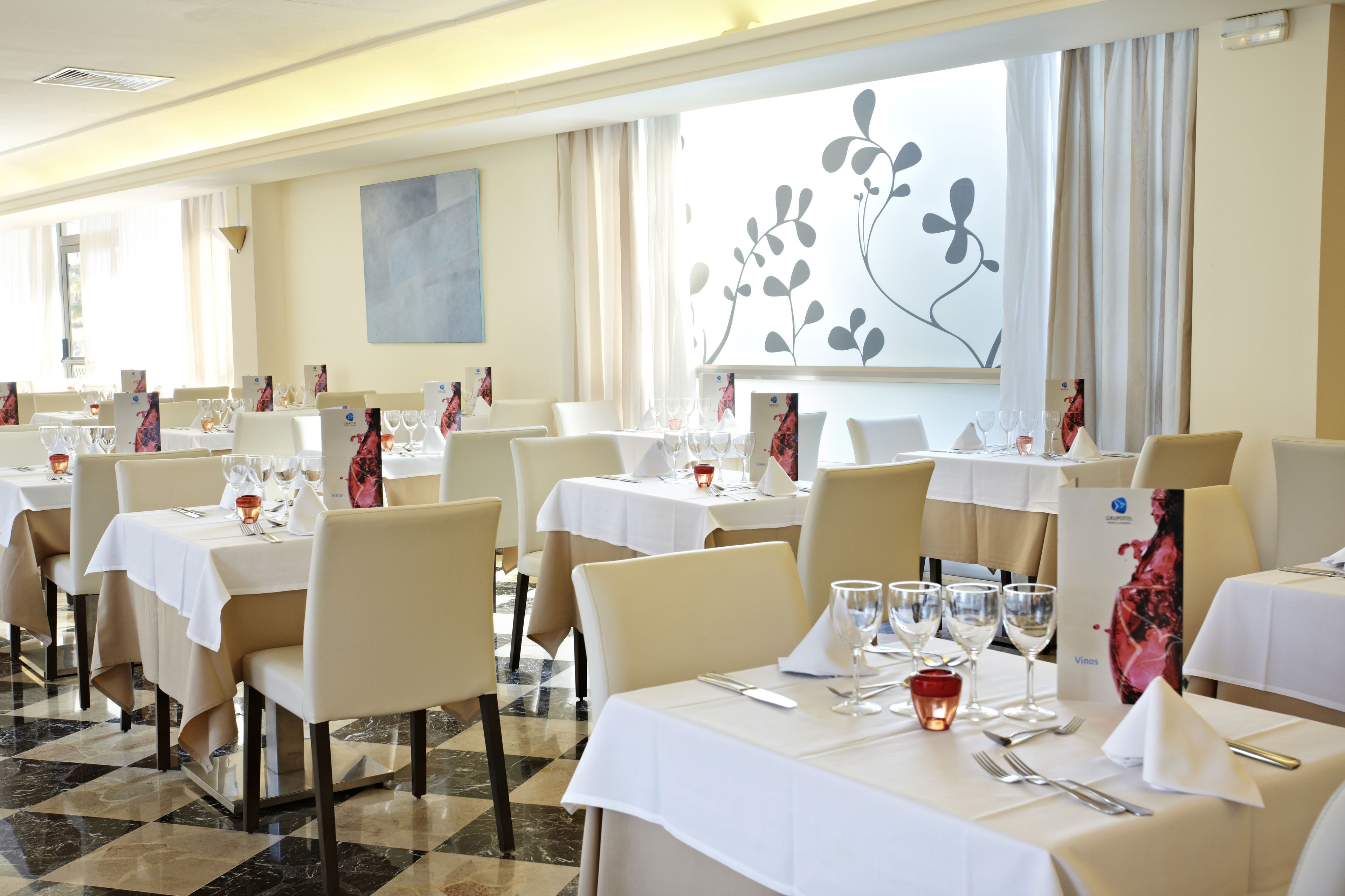 A restaurant with multiple tables set for dining, featuring white tablecloths and beige chairs.
