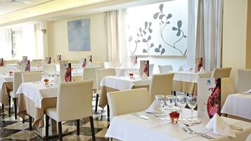 A restaurant with multiple tables set for dining, featuring white tablecloths and beige chairs.