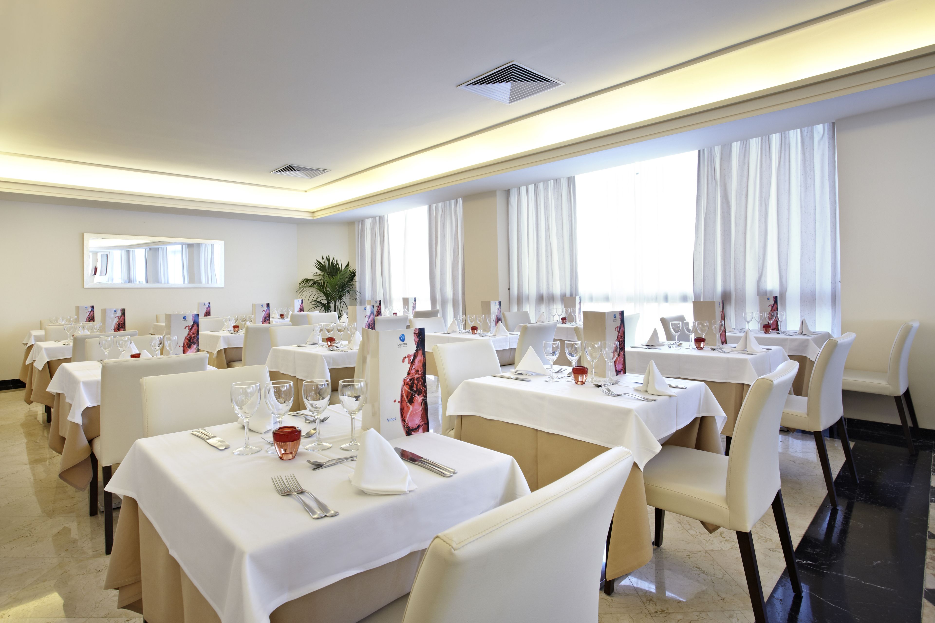 Un espace repas comprenant plusieurs tables, chacune recouverte d’une nappe blanche et agrémentée de chaises et de couverts.