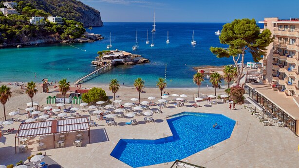 Un resort con piscina, zona de playa y vistas al mar con barcos.
