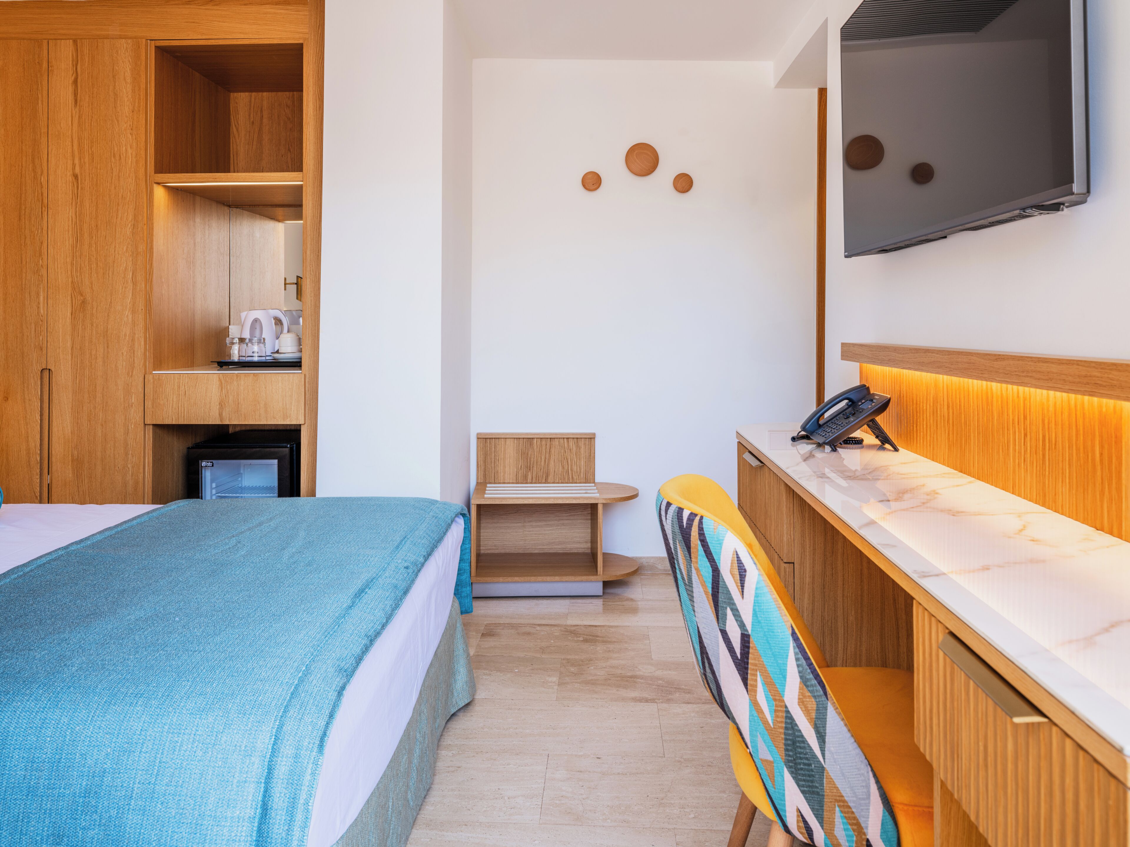 A hotel room with a bed, a desk, a chair, a TV, and a minibar.