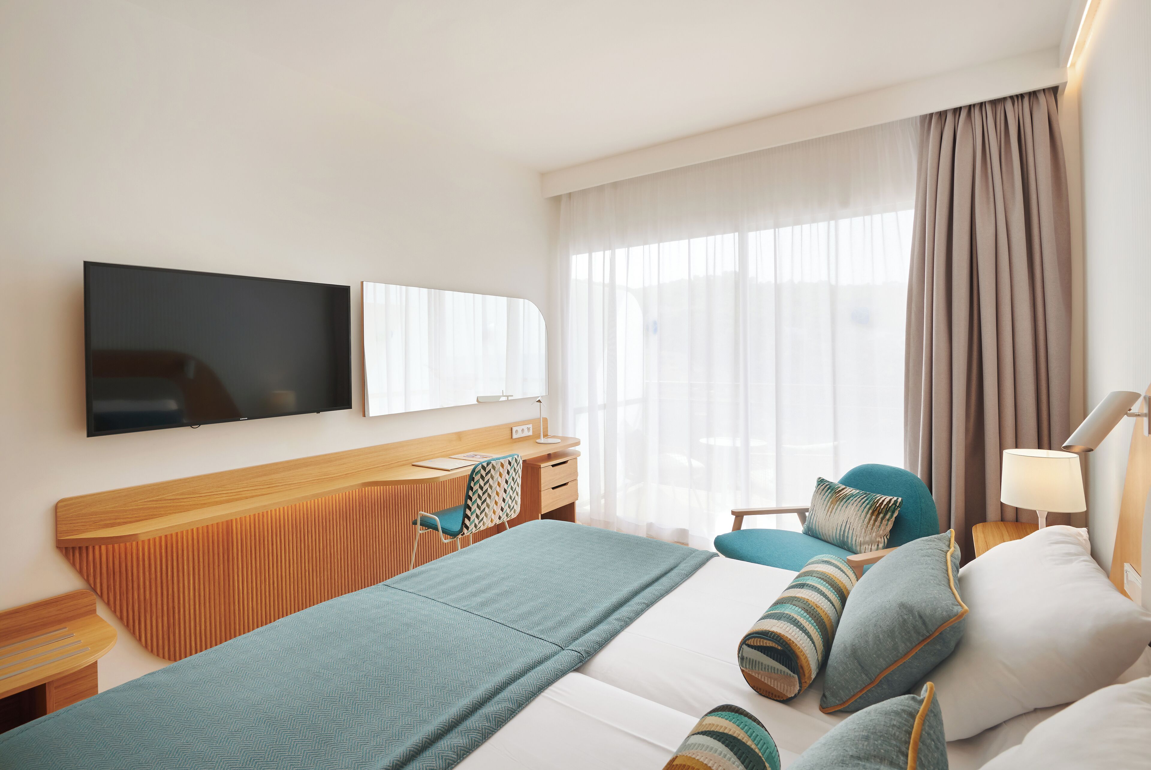 A hotel room with a bed, a desk, a chair, a TV, and a window with curtains.