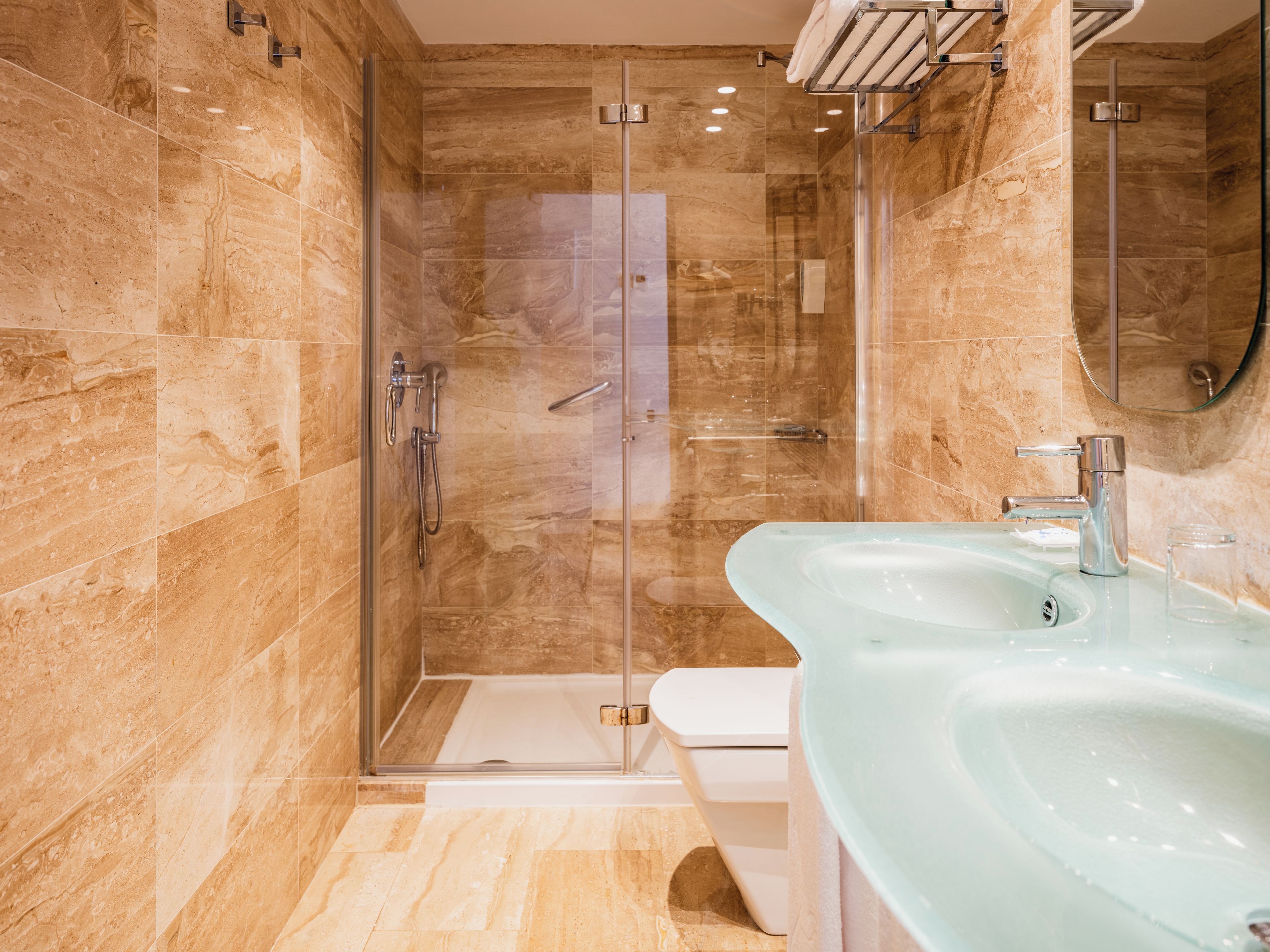 Un baño moderno con ducha envuelta en vidrio, un lavamanos espacioso de vidrio y un inodoro.