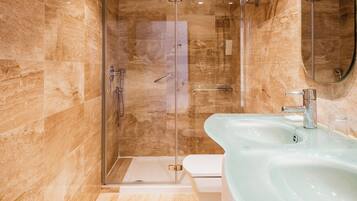 Un baño moderno con ducha envuelta en vidrio, un lavamanos espacioso de vidrio y un inodoro.