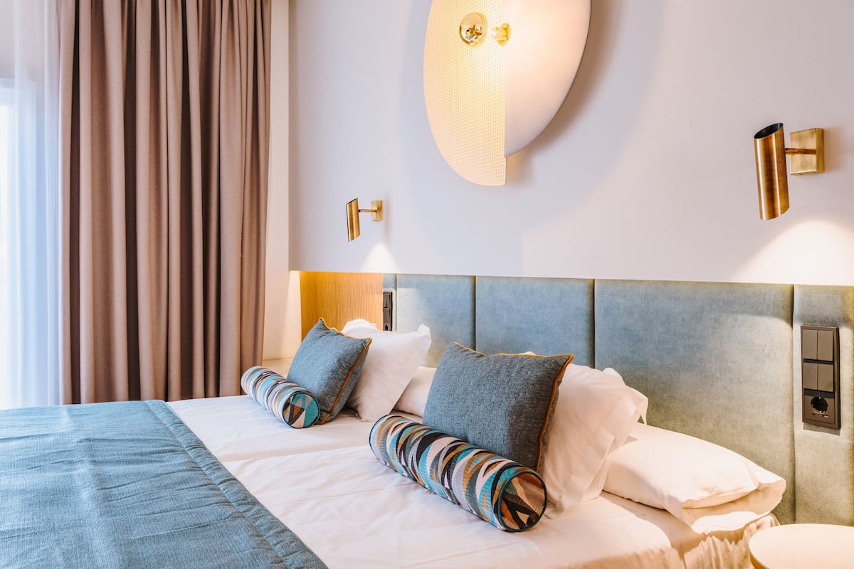 Una habitación de hotel con una cama grande, un cabecero, una mesita de noche y una lámpara fijada a la pared.