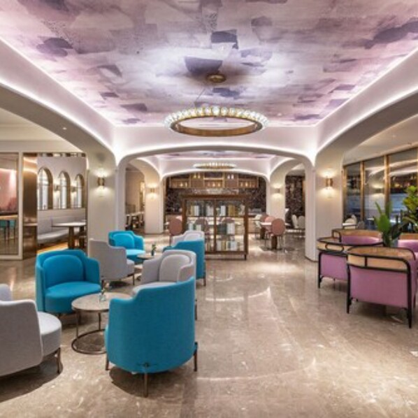 A modern lobby with a marble floor, blue and grey armchairs, and a central seating area with a circular light fixture.