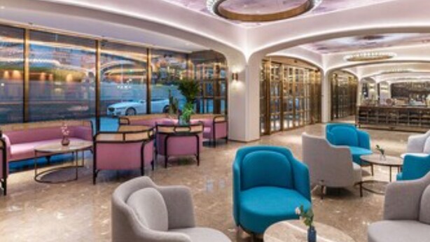 Een moderne lounge met zitplaatsen en tafels, grote ramen met uitzicht op de stad en een opvallend plafondontwerp.