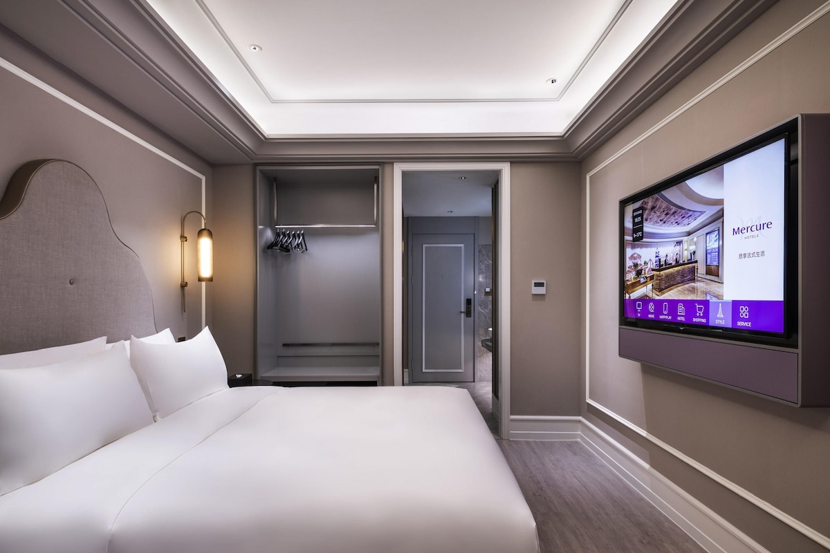 A hotel room with a large bed, a walk-in closet, a shower, and a television displaying hotel information.