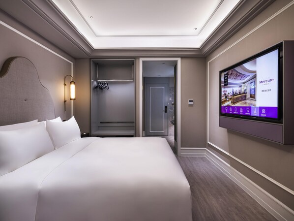 A hotel room with a large bed, a walk-in closet, a shower, and a television displaying hotel information.
