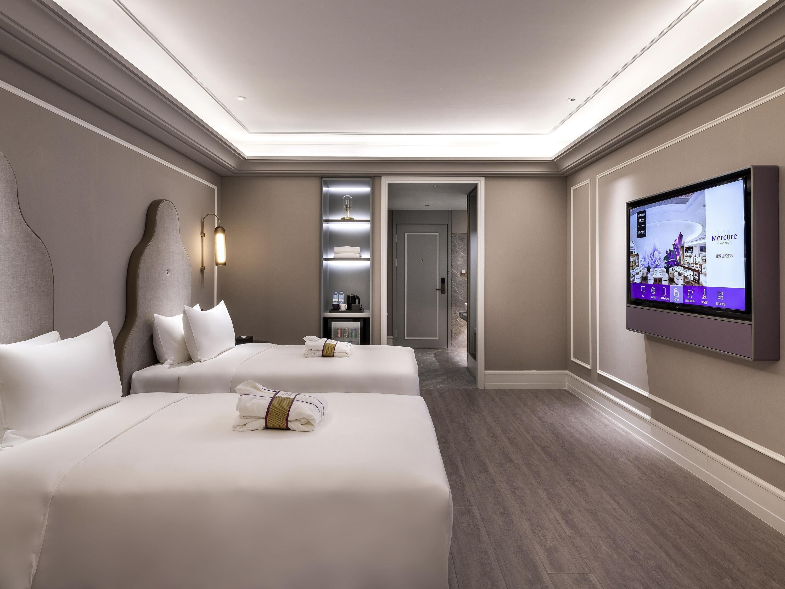 Ein Hotelzimmer mit zwei Betten, einem Fernseher, einer Minibar und einem durchgegangenen Badezimmer.