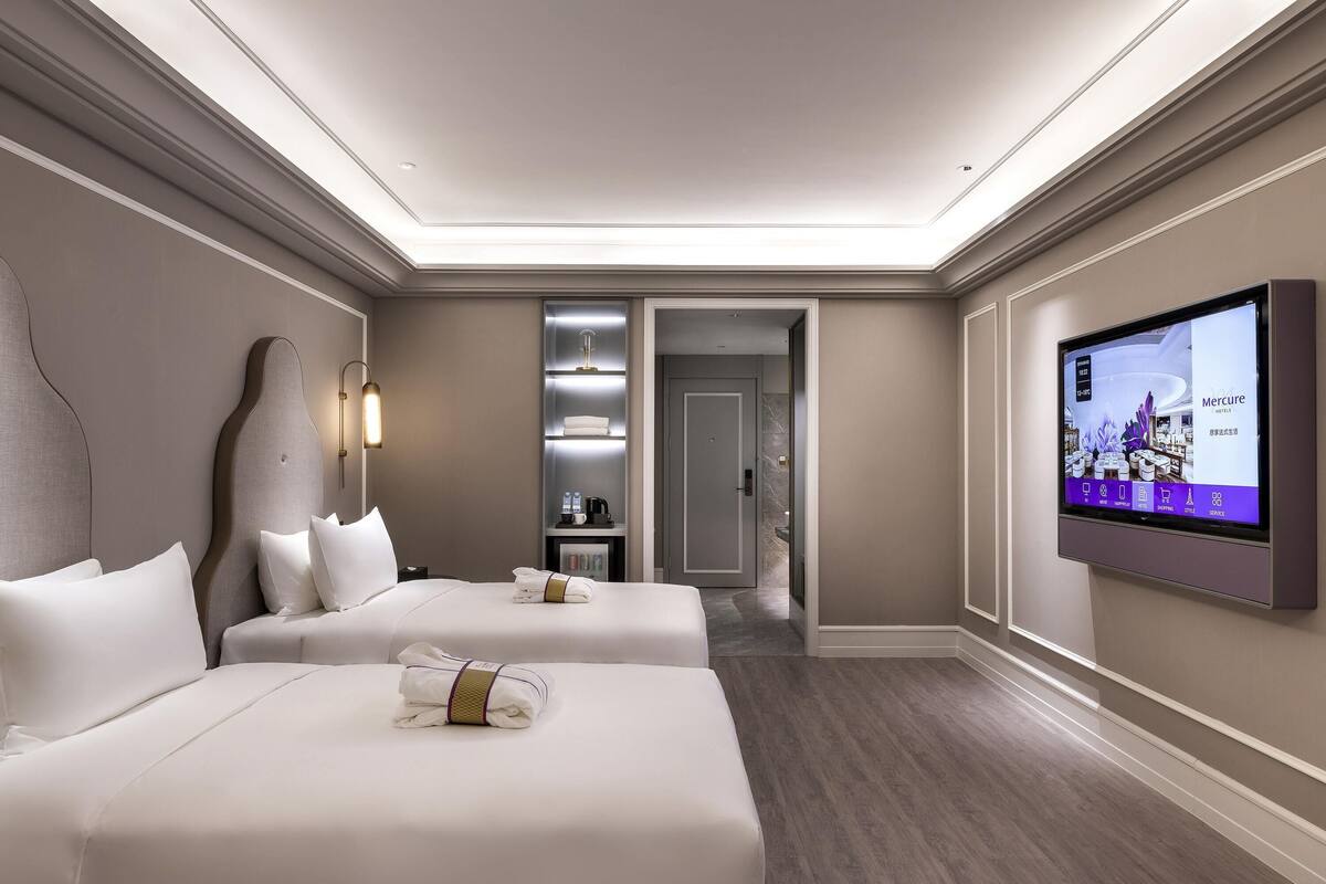 Une chambre d’hôtel avec deux lits, une télévision, un minibar et une salle de bain visible à travers une porte ouverte.