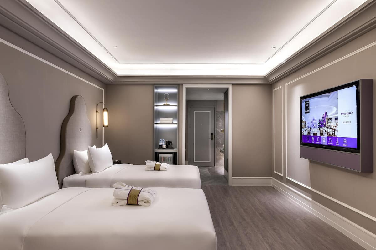 Ein Hotelzimmer mit zwei Betten, einem Fernseher, einer Minibar und einem durchgegangenen Badezimmer.