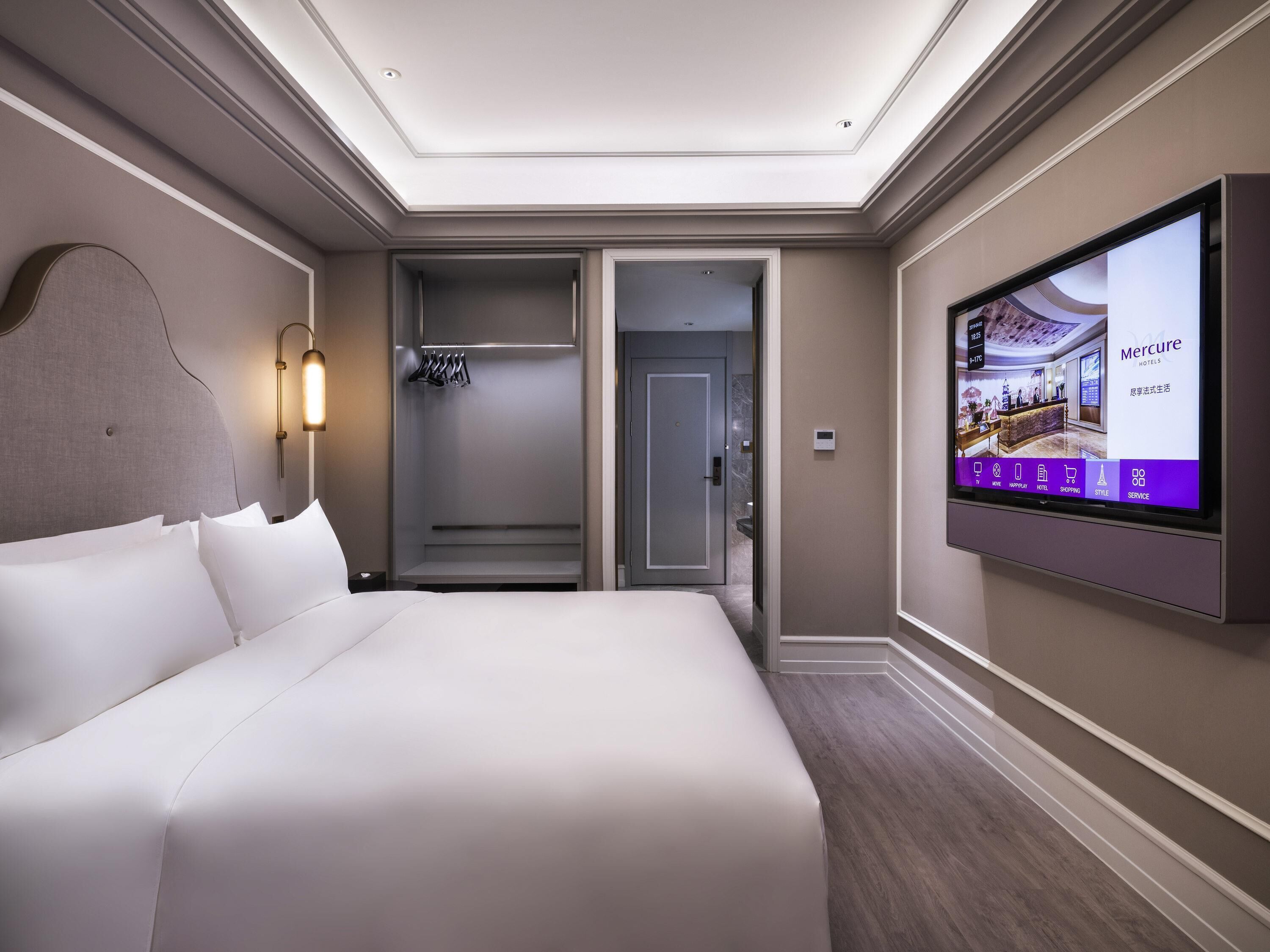 Ein Hotelzimmer mit einem großen Bett, einem begehbaren Kleiderschrank, einer Dusche und einem Fernseher, der Hotelinformationen zeigt.