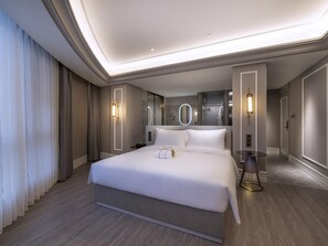 Quarto de hotel moderno com uma cama grande, uma mesa de cabeceira, um espelho e um banheiro visível por uma porta aberta.