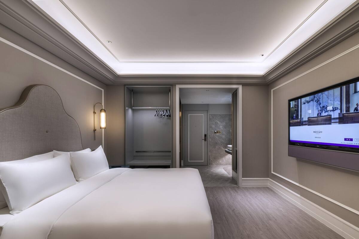 Une chambre d’hôtel avec un grand lit, une télévision, une armoire et une salle de bain visible à travers une porte ouverte.