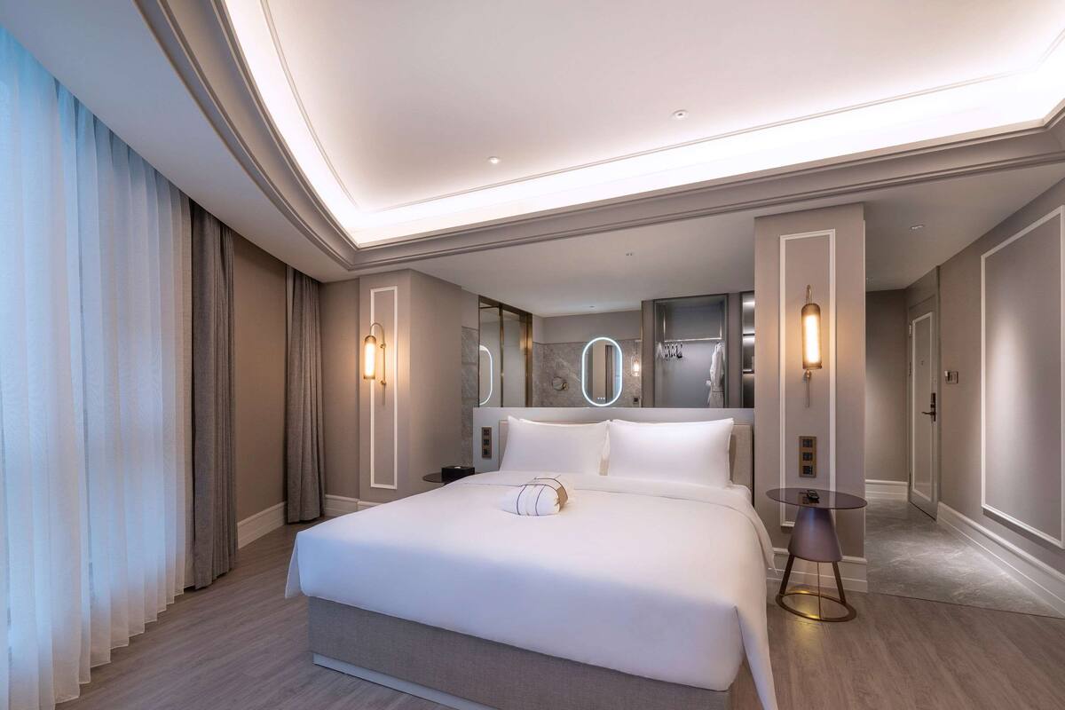 Een moderne hotelkamer met een groot bed, een nachtkastje en een spiegel met verlichting.