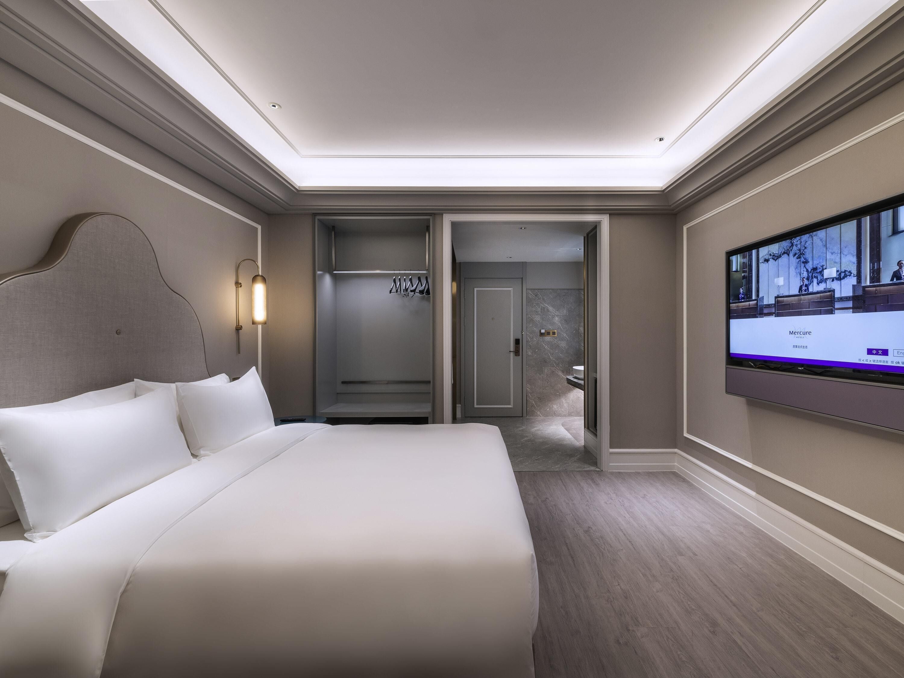 Ein Hotelzimmer mit einem großen Bett, einem Fernseher, einem Kleiderschrank und einem durch eine geöffnete Tür einsehbaren Badezimmer.