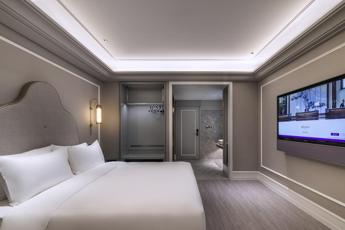 Ein Hotelzimmer mit einem großen Bett, einem Fernseher, einem Kleiderschrank und einem durch eine geöffnete Tür einsehbaren Badezimmer.