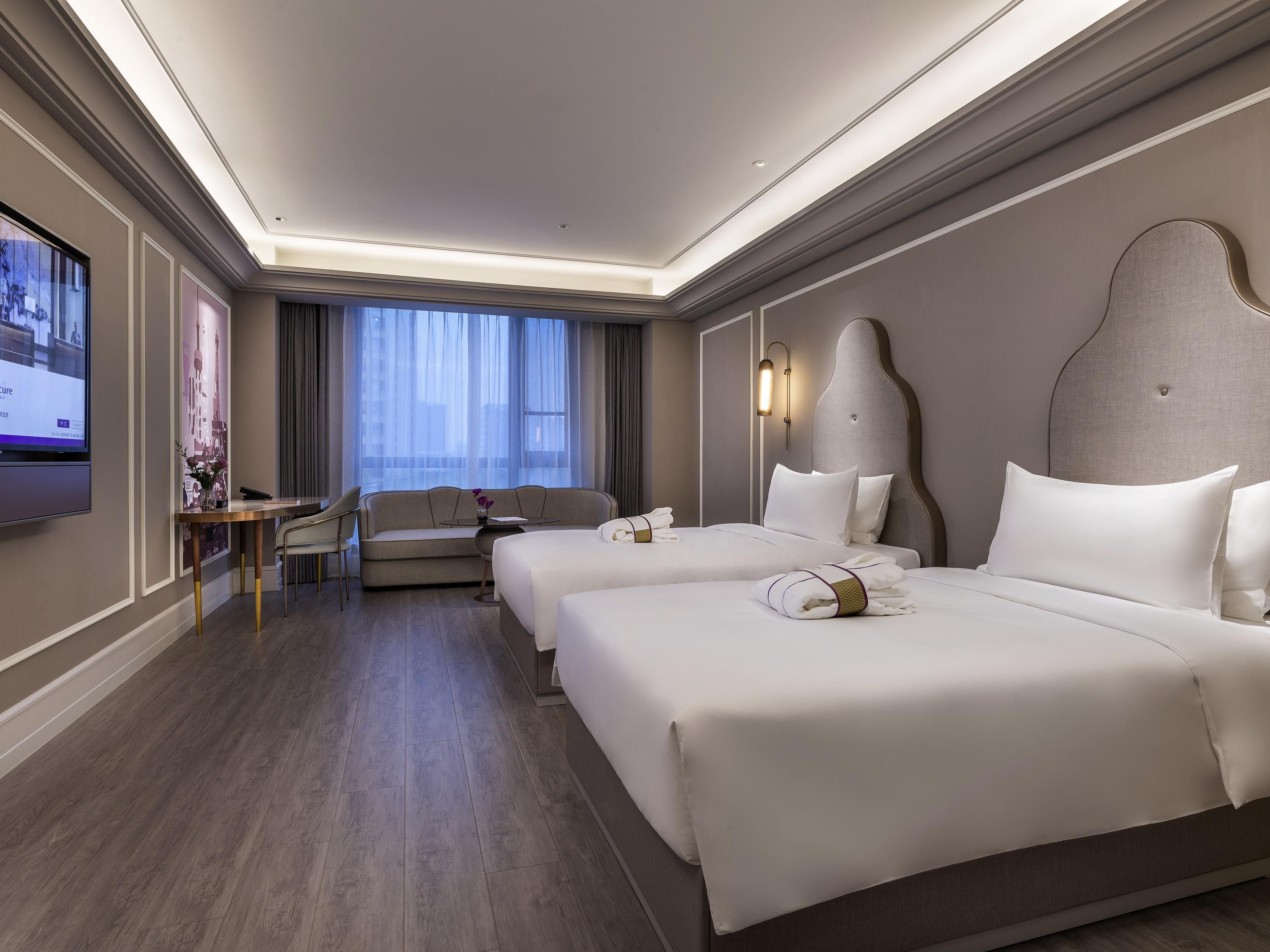 A hotel room with two beds, a sofa, a TV, and a large window.