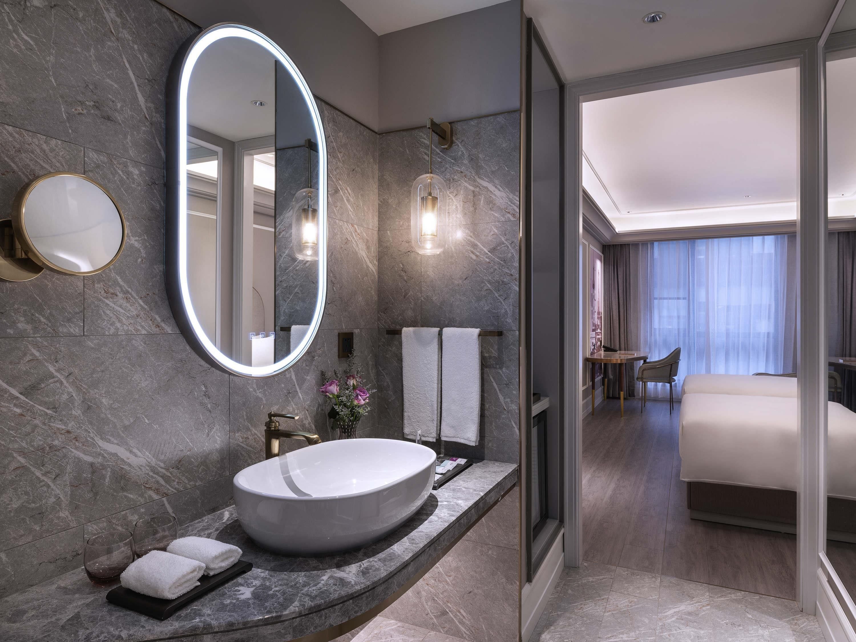 A modern bathroom with a large oval sink, a round mirror, and a glass-enclosed shower.