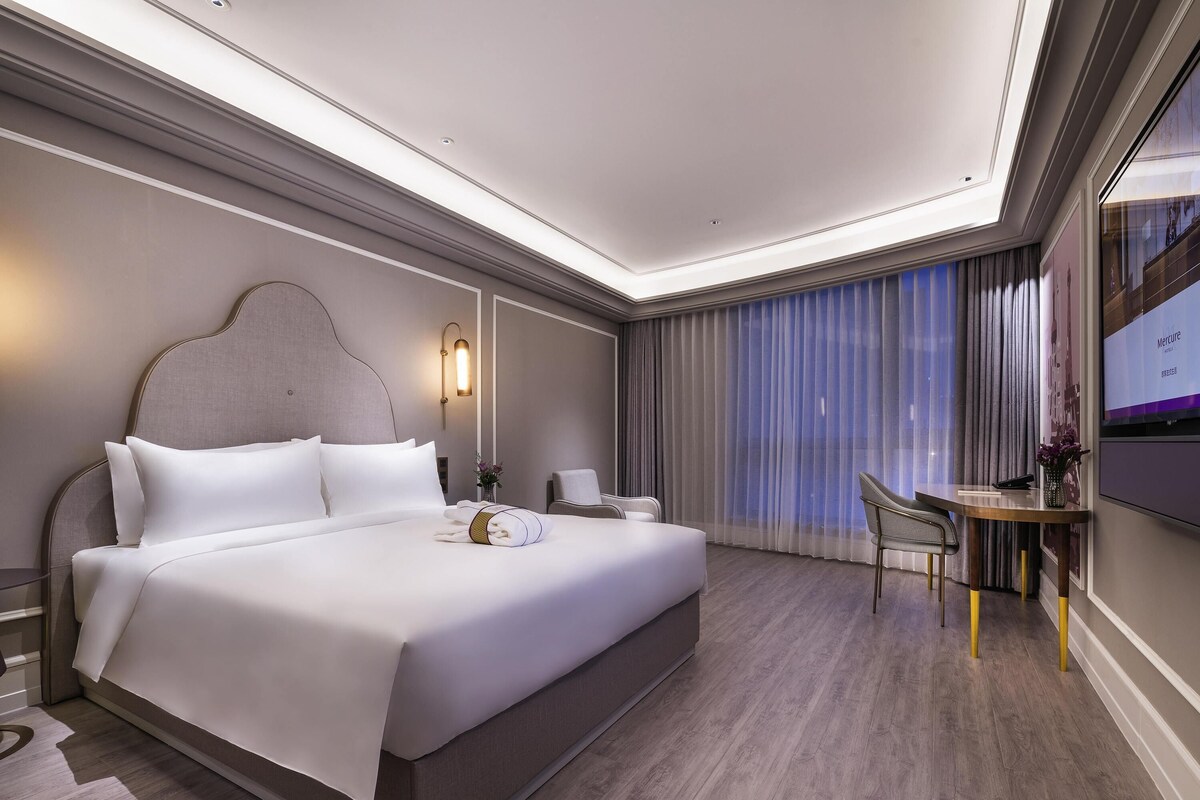 Quarto de hotel moderno com uma cama grande, uma escrivaninha e uma televisão.