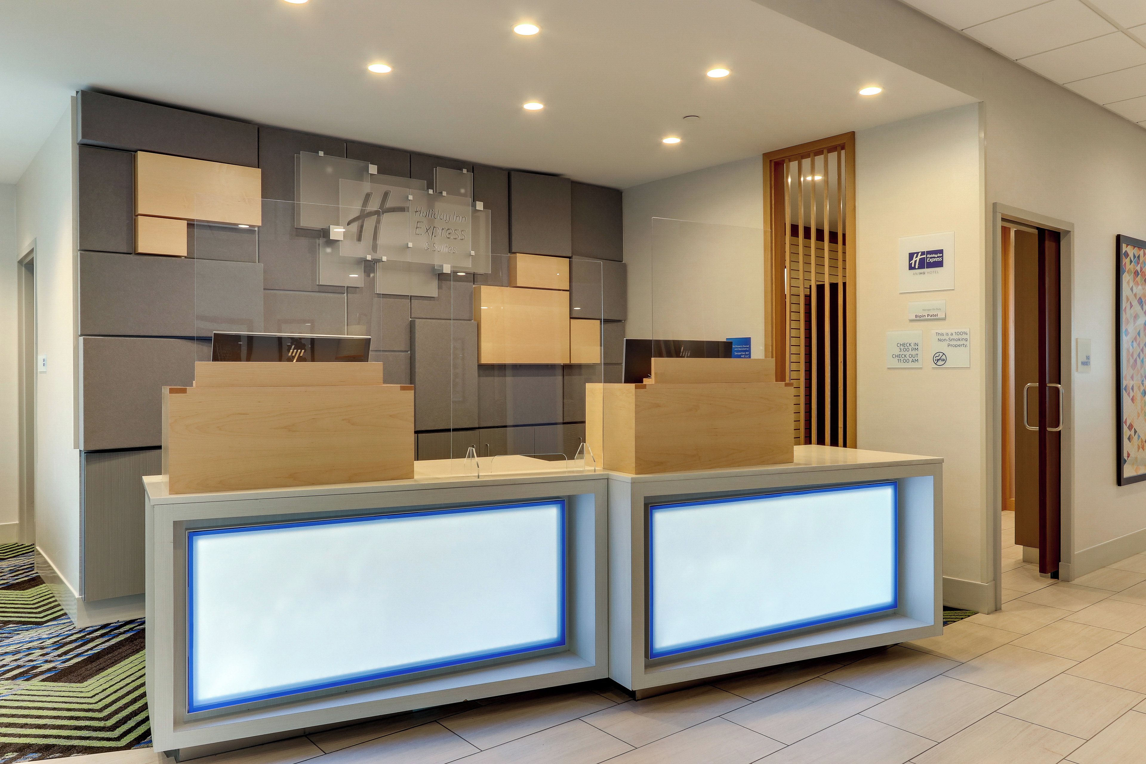 A reception desk with a modern design, featuring two illuminated panels and a wall-mounted sign indicating the property is a Holiday Inn Express & Suites.