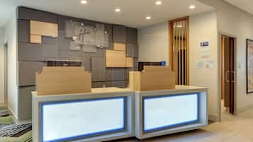 A reception desk with a modern design, featuring two illuminated panels and a wall-mounted sign indicating the property is a Holiday Inn Express & Suites.