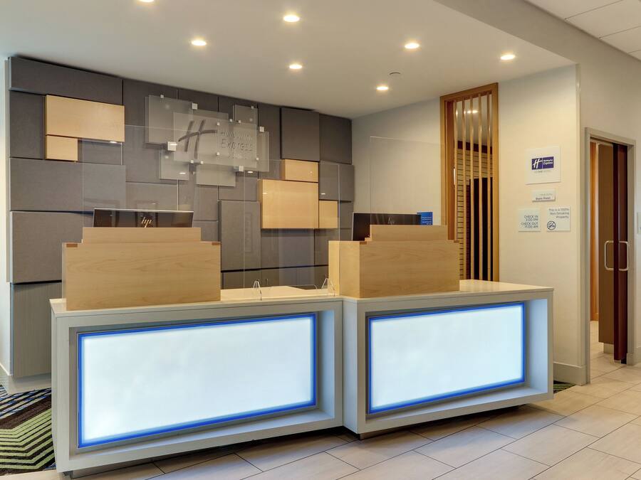 A reception desk with a modern design, featuring two illuminated panels and a wall-mounted sign indicating the property is a Holiday Inn Express & Suites.