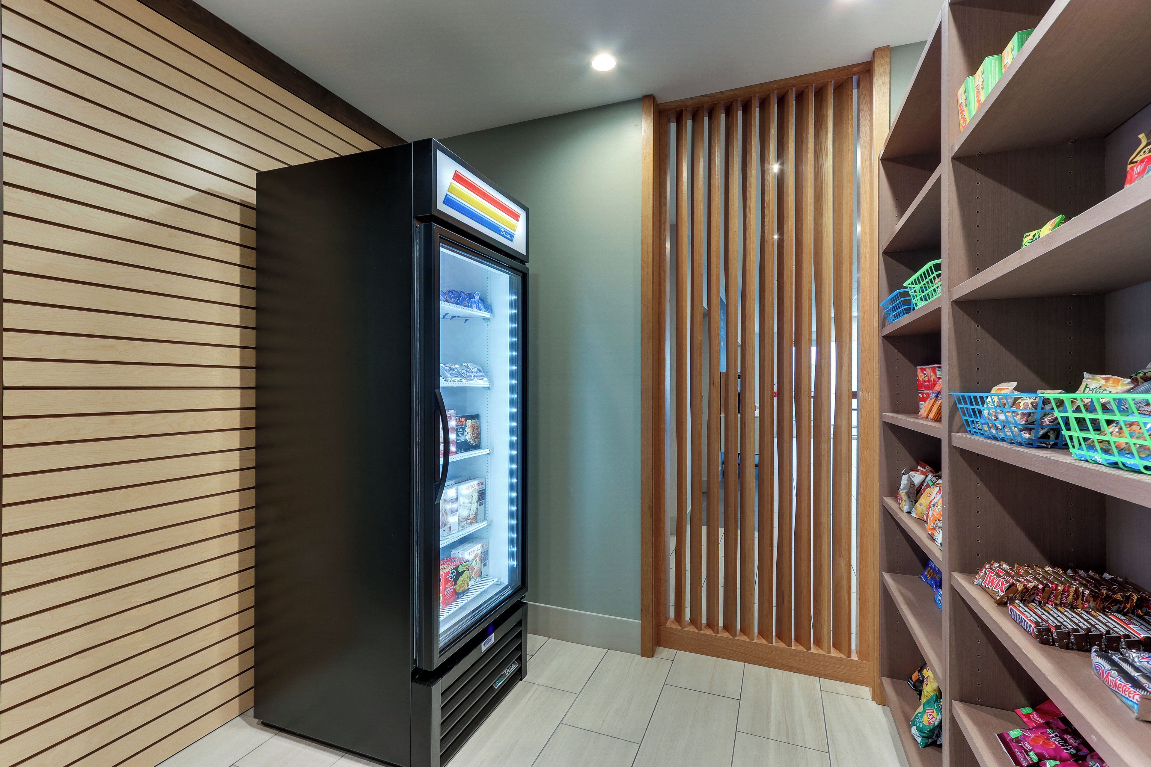 A self-service beverage dispenser with a variety of drinks, adjacent to a snack shelf stocked with various packaged goods.