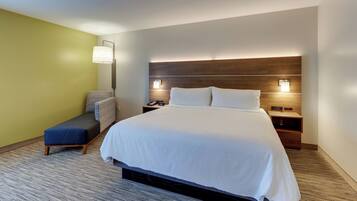Una habitación de hotel con una cama grande, mesitas de noche, un banco y una lámpara de pared.