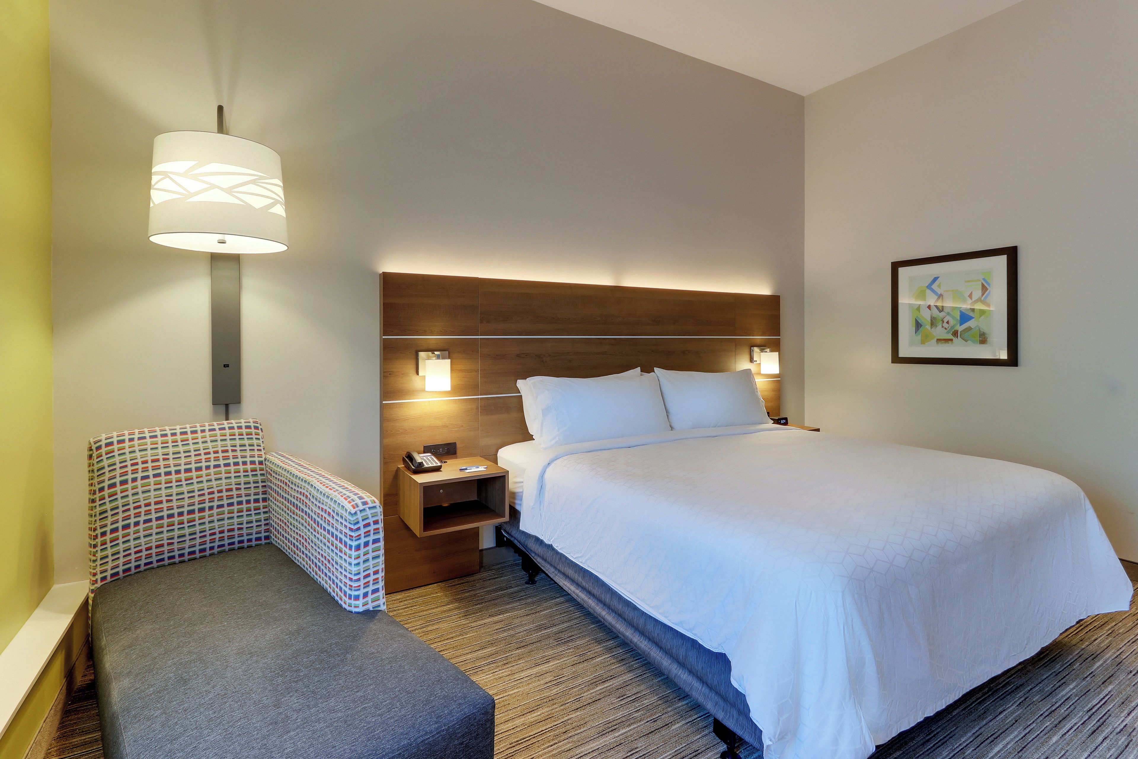 A hotel room with a bed, a nightstand, a telephone, a lamp, and a framed picture on the wall.