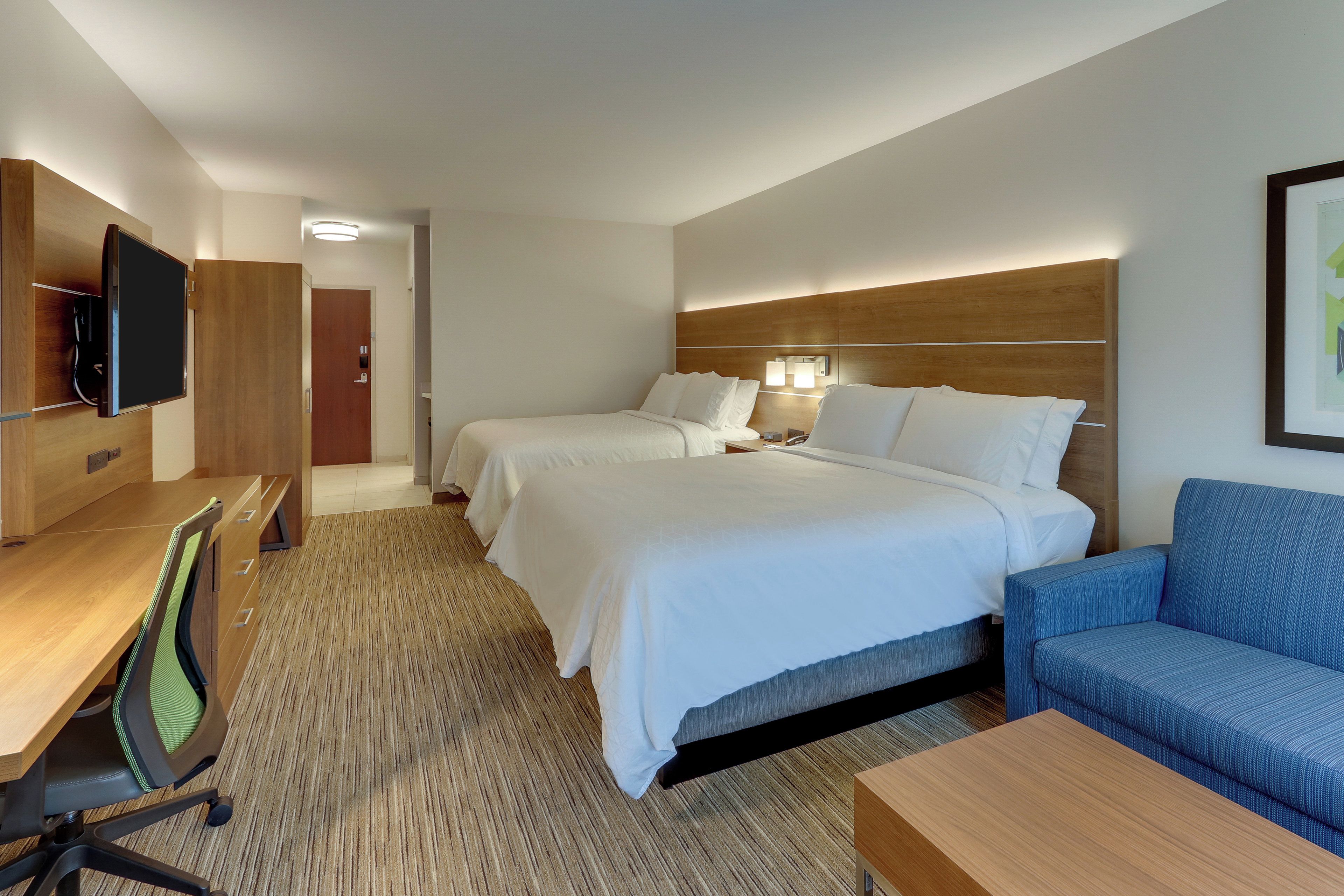 A hotel room with two beds, a desk, a chair, a TV, and a sofa.