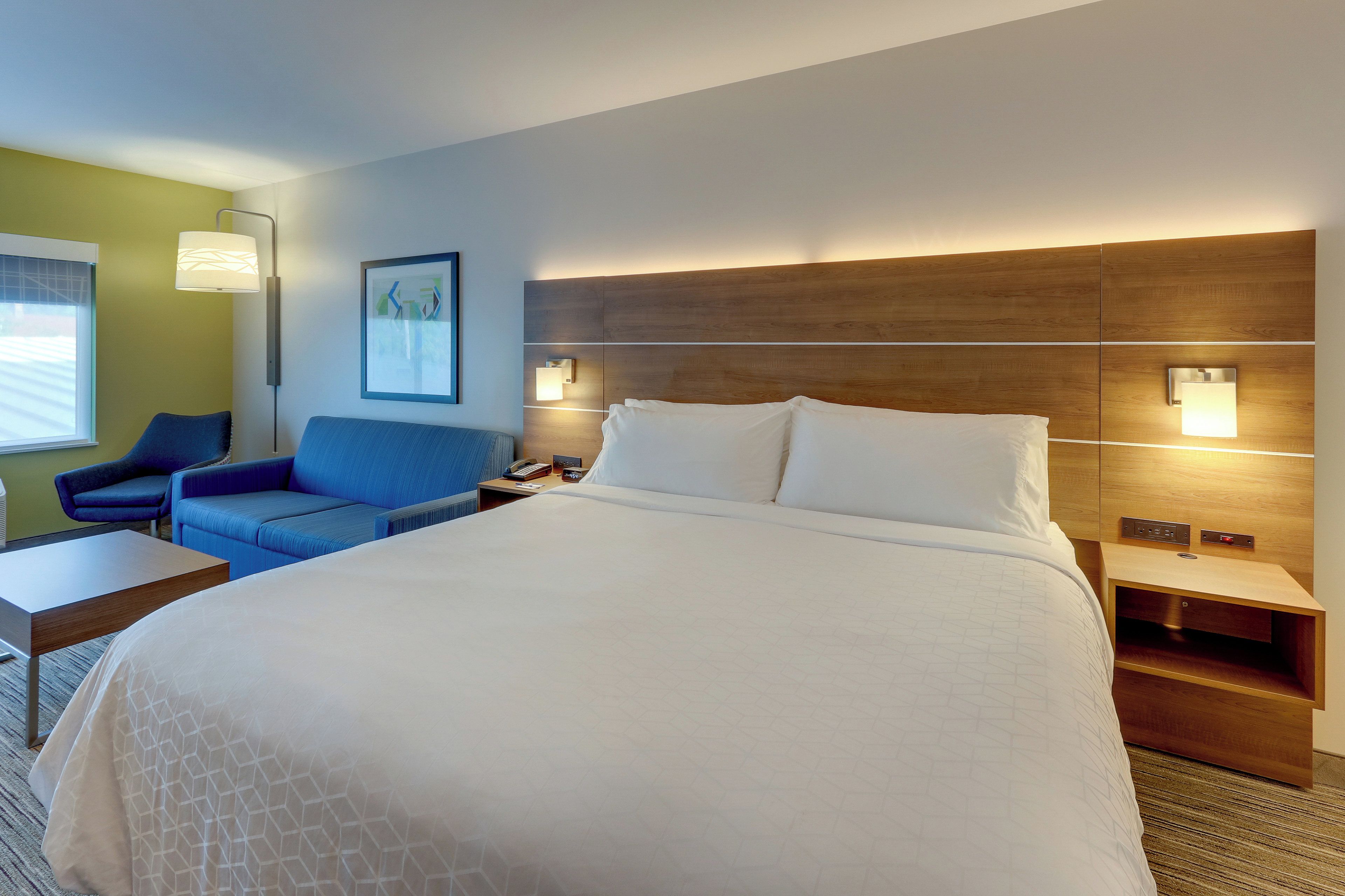 A hotel room with a large bed, a desk, a chair, and a nightstand.