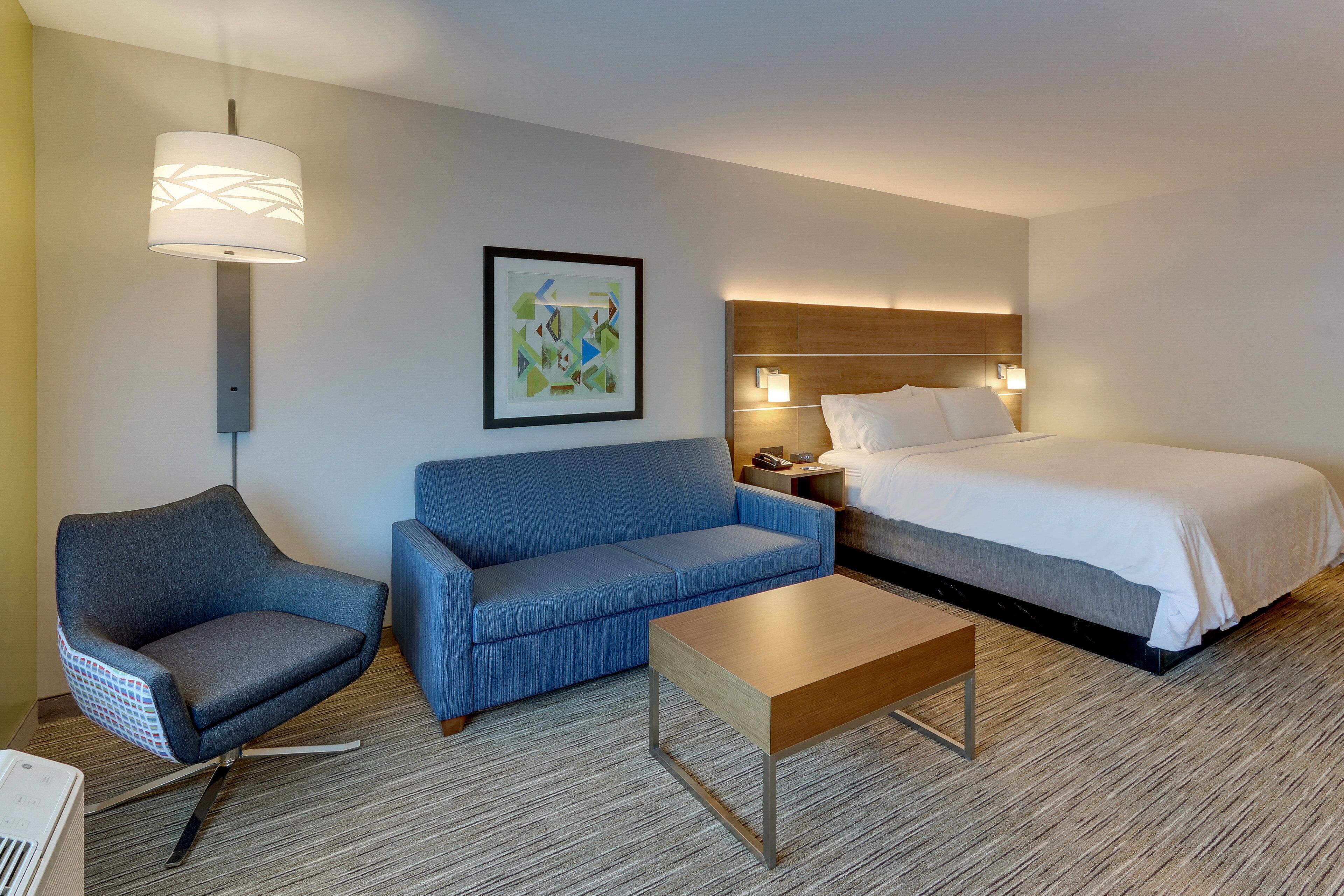Une chambre d’hôtel comprenant un lit, un canapé, une chaise, une petite table et une lampe fixée au mur.