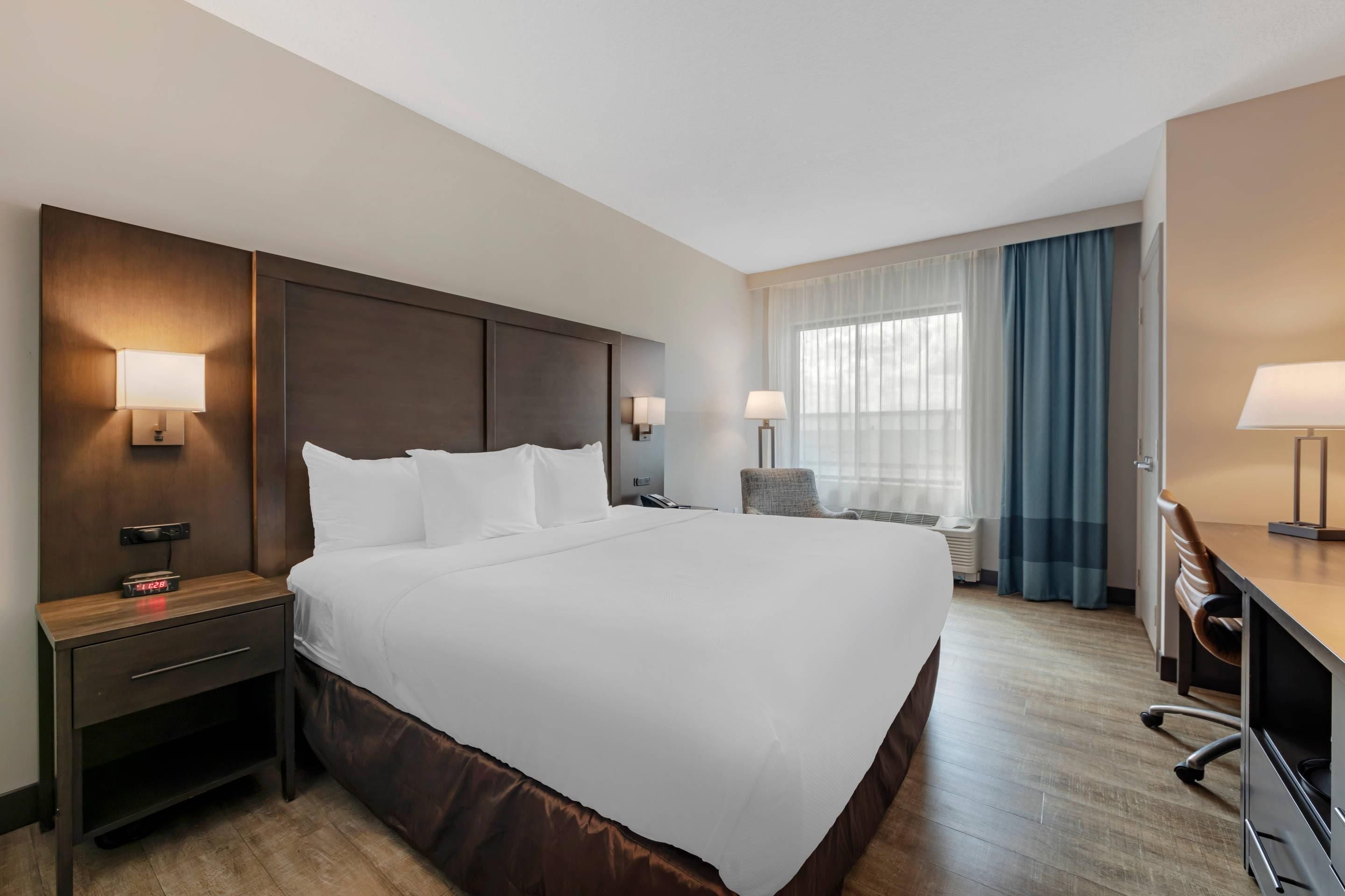 Quarto de hotel com uma cama grande, mesas de cabeceira com abajures, uma escrivaninha e uma cadeira.