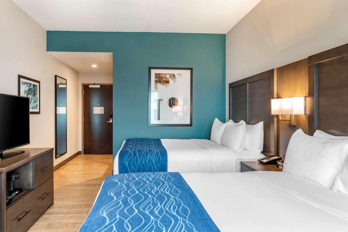 A hotel room with two beds, a TV, a desk, and a mirror.