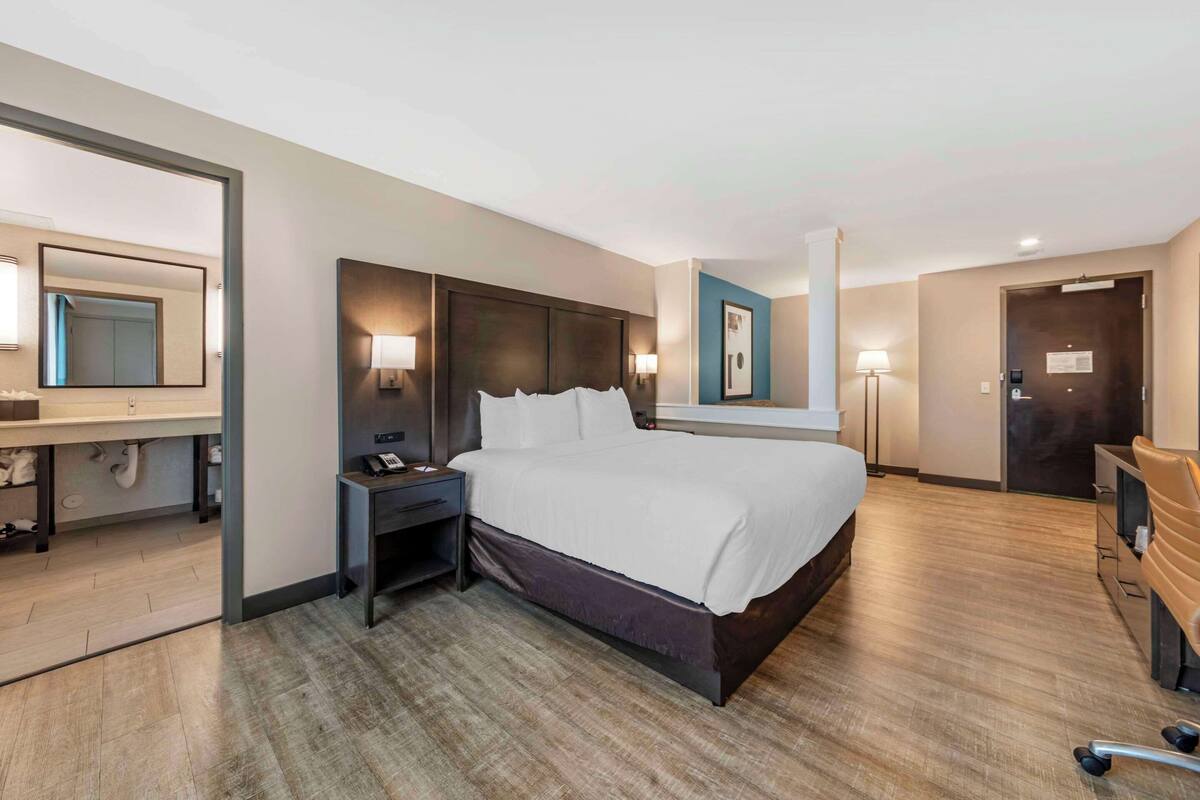 A hotel room with a large bed, bedside tables, a desk, a chair, and a mirror.