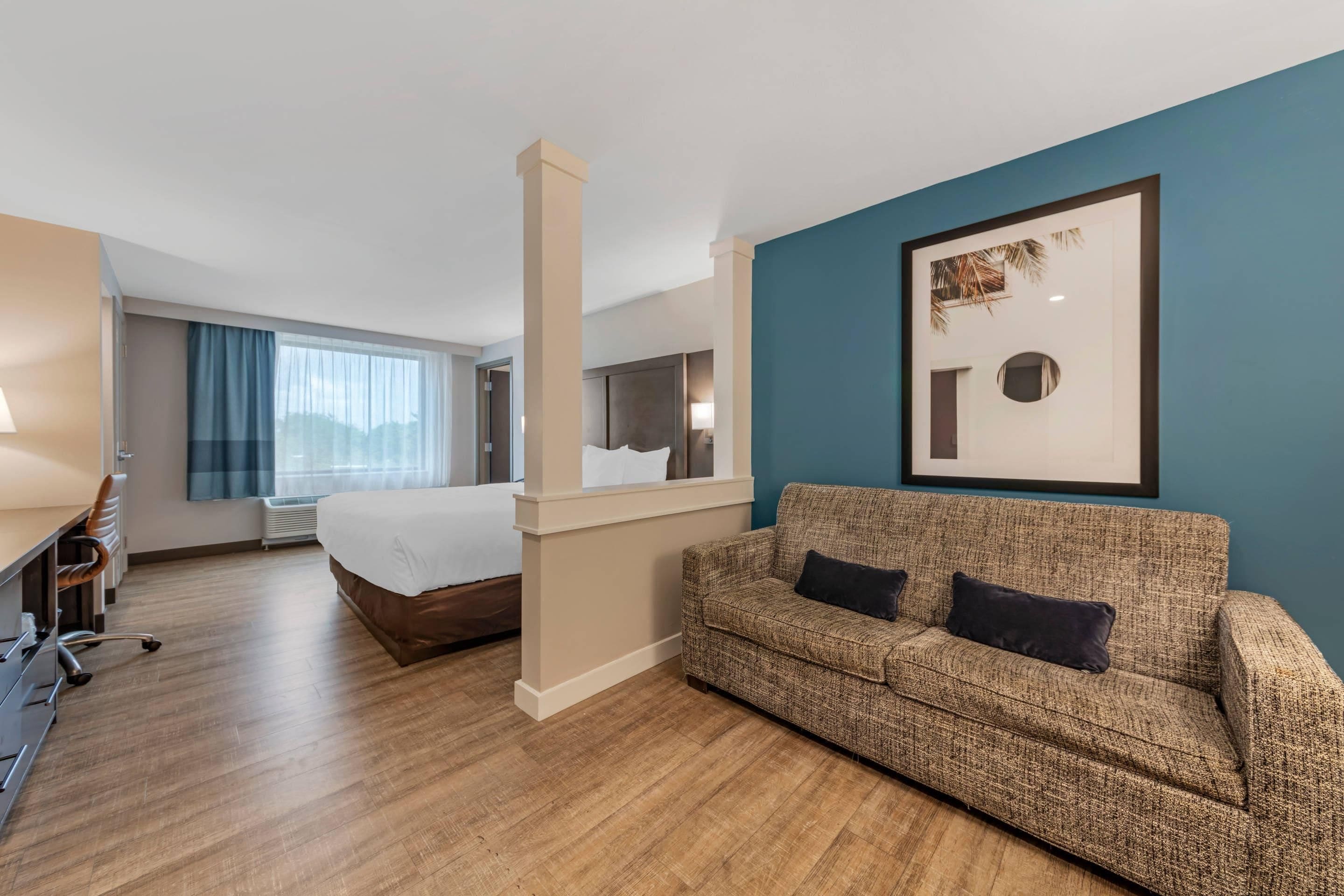 Una habitación de hotel con cama, sofá, escritorio y un ventanal grande.