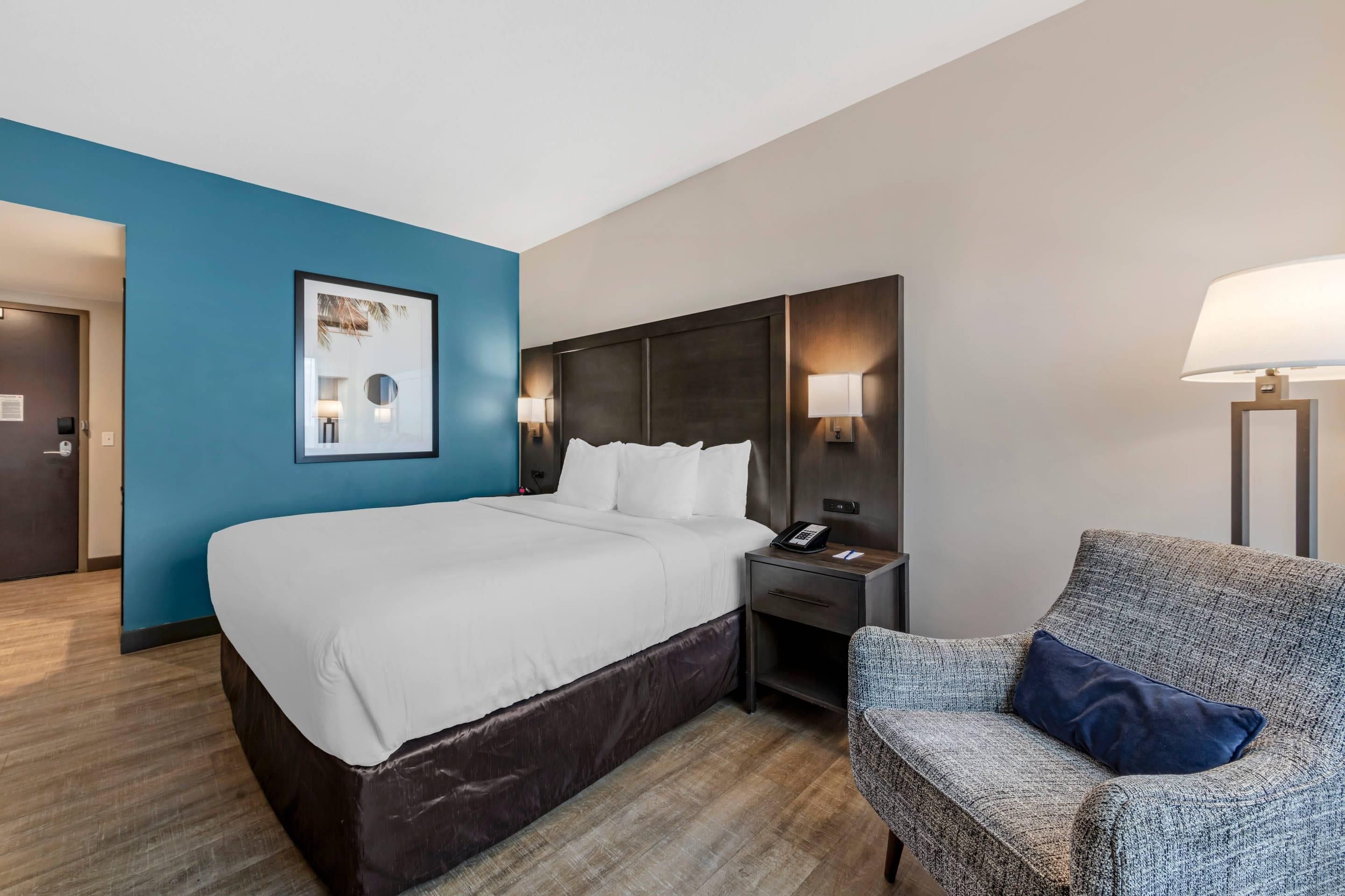 Une chambre d’hôtel avec un lit, une chaise, une table de chevet et une lampe fixée au mur.