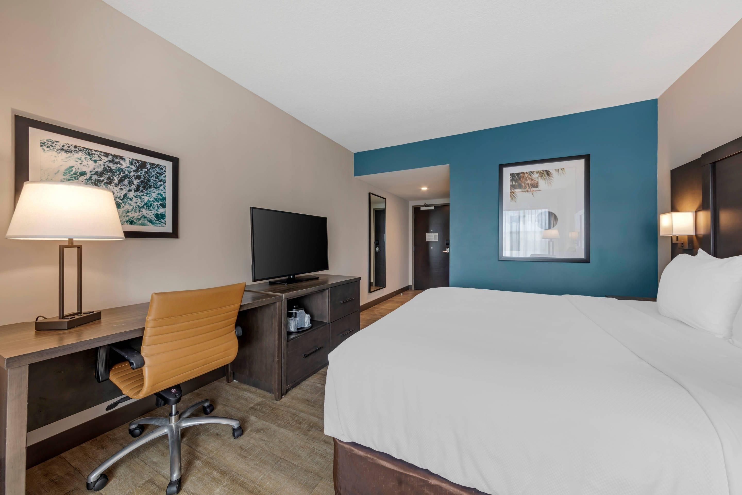 A hotel room with a bed, desk, chair, television, and artwork.