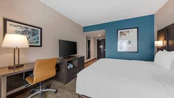 A hotel room with a bed, desk, chair, television, and artwork.
