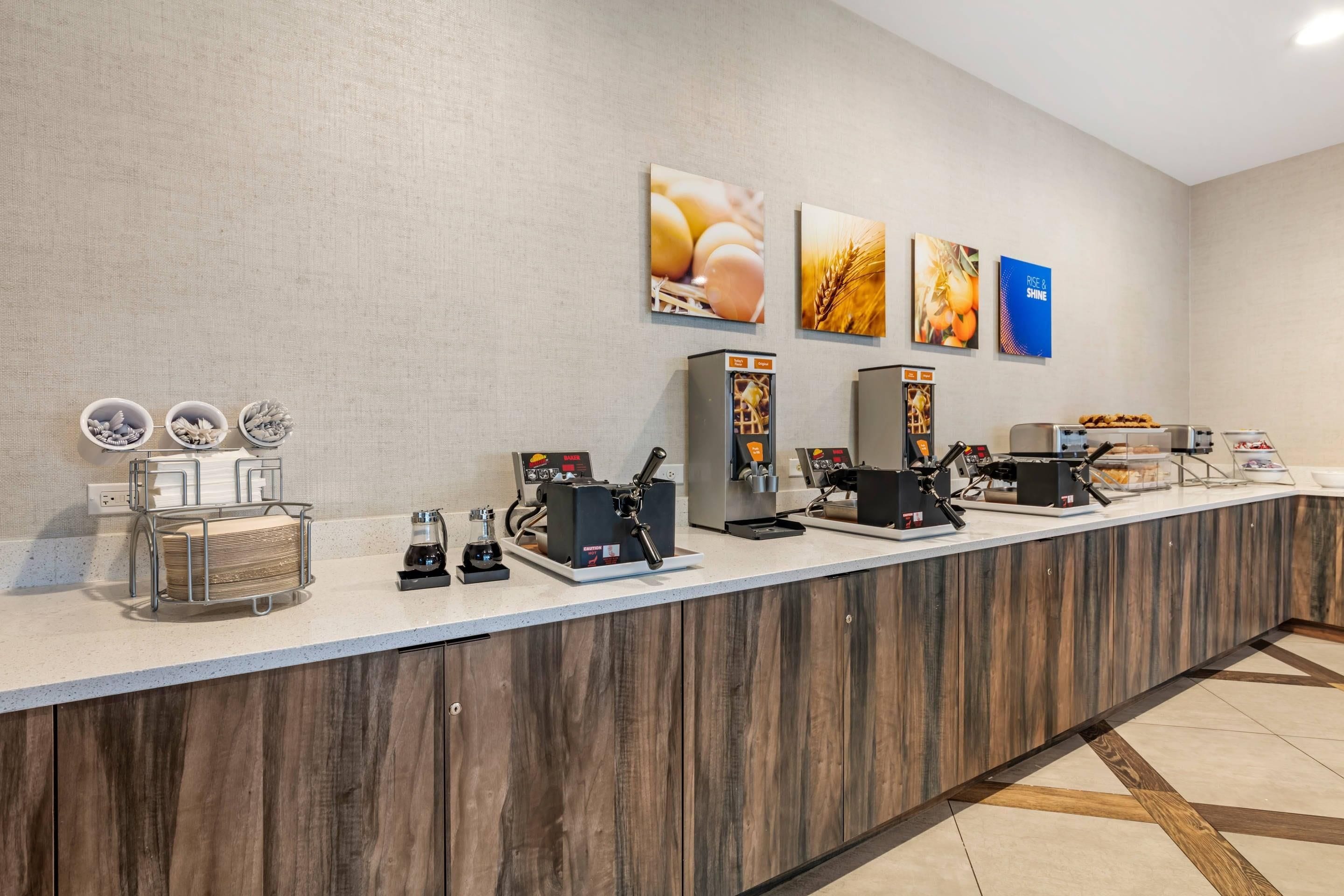 Zona de desayuno autoservicio con máquinas de café, una variedad de pan y un bol de fruta.