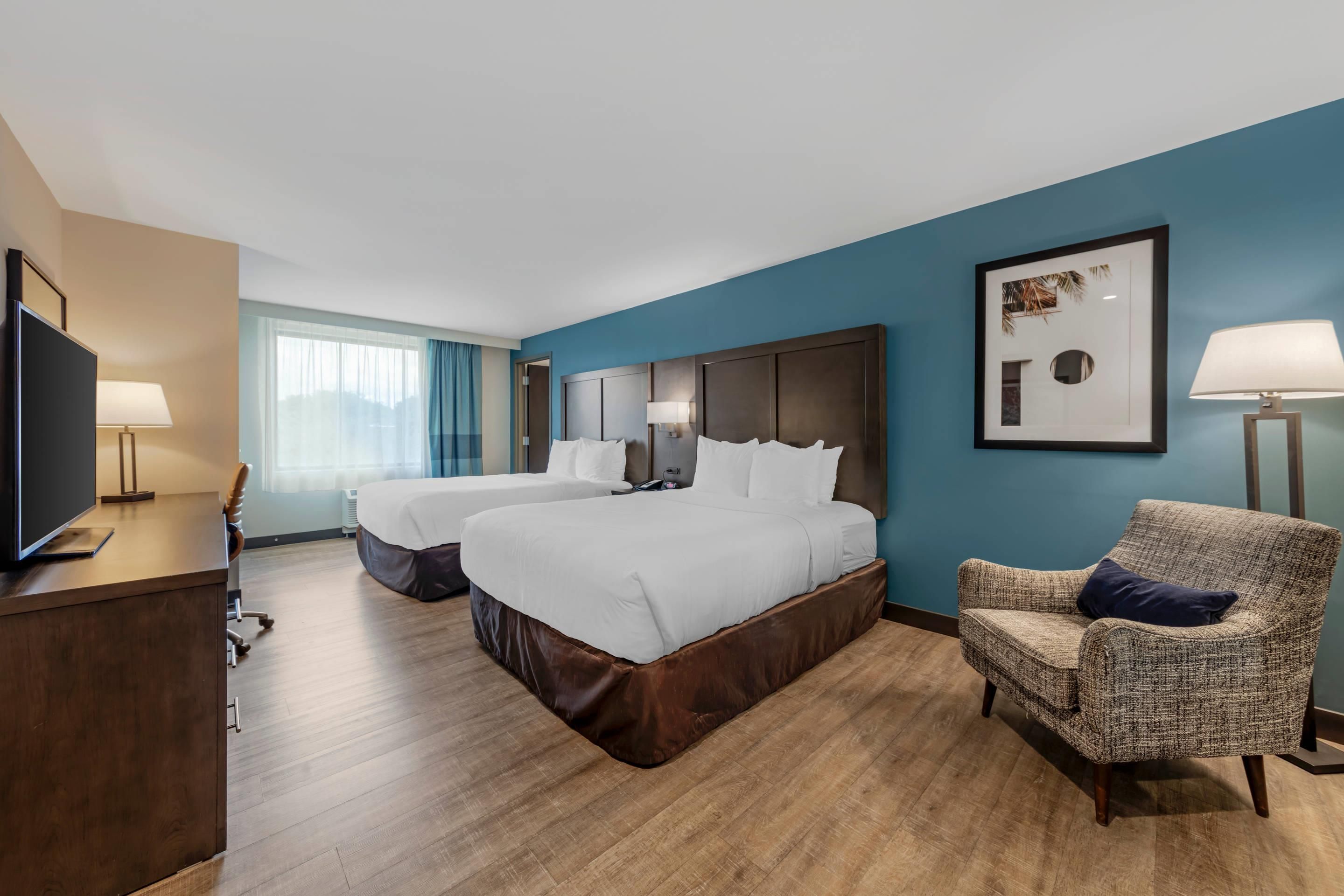 Une chambre d’hôtel avec deux lits, un bureau doté d’un téléviseur à écran plat, une chaise et une grande fenêtre.