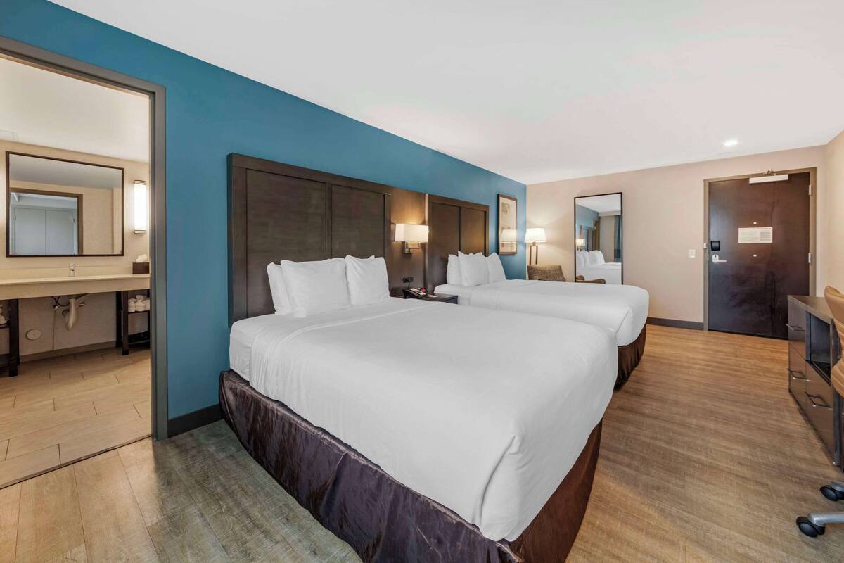 A hotel room with a large bed, a desk, a chair, and a mirror.