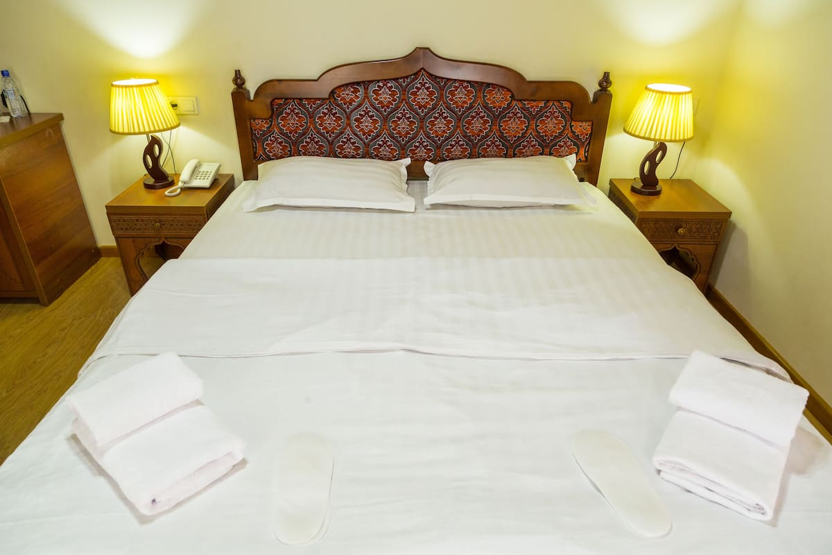 Una cama bien tendida con sábanas blancas, dos lámparas de noche y un cabecero de madera con un diseño estampado.