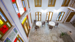 A courtyard with a round table and chairs, surrounded by large windows with wooden frames. - Hotel Volida Boutique (Bukhara)