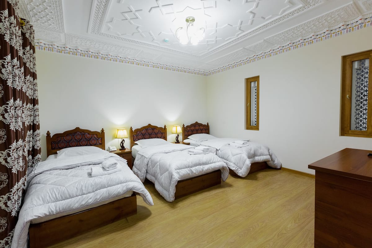 Habitación de hotel con dos camas, cabeceros de madera, ropa de cama blanca y un escritorio de madera.